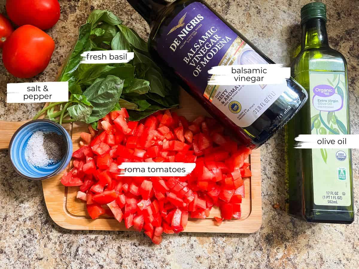 Bruschetta ingredients labeled on a wooden cutting board and counter.