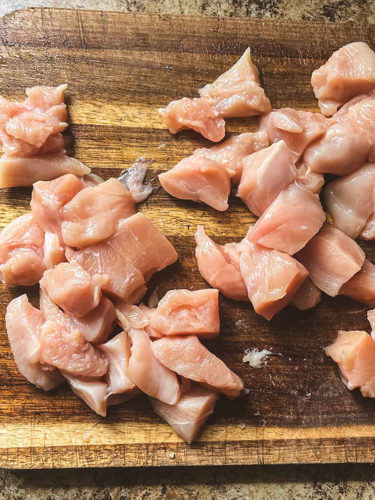 Cubes of raw chicken on a wooden cutting board.