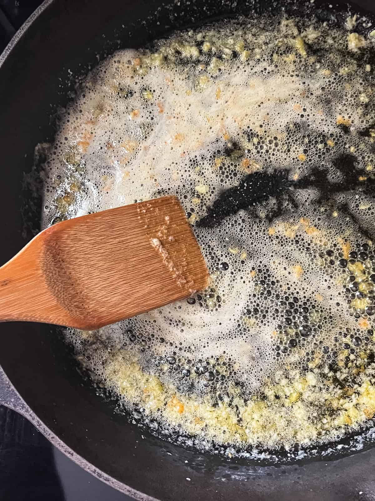 Cooking garlic in a cast iron skillet with some butter and stirring it with a wooden spoon.