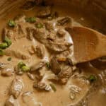 Dutch oven beef stroganoff being served with a wooden spoon.