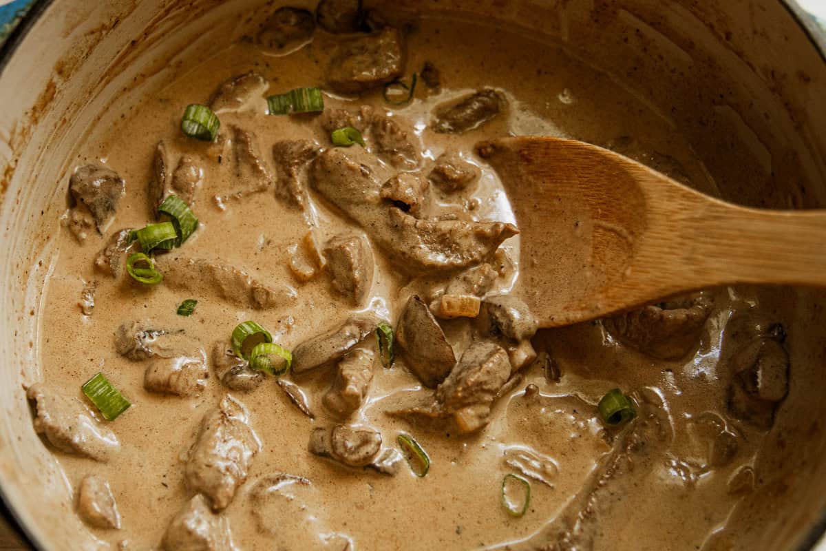 Dutch oven beef stroganoff being served with a wooden spoon.
