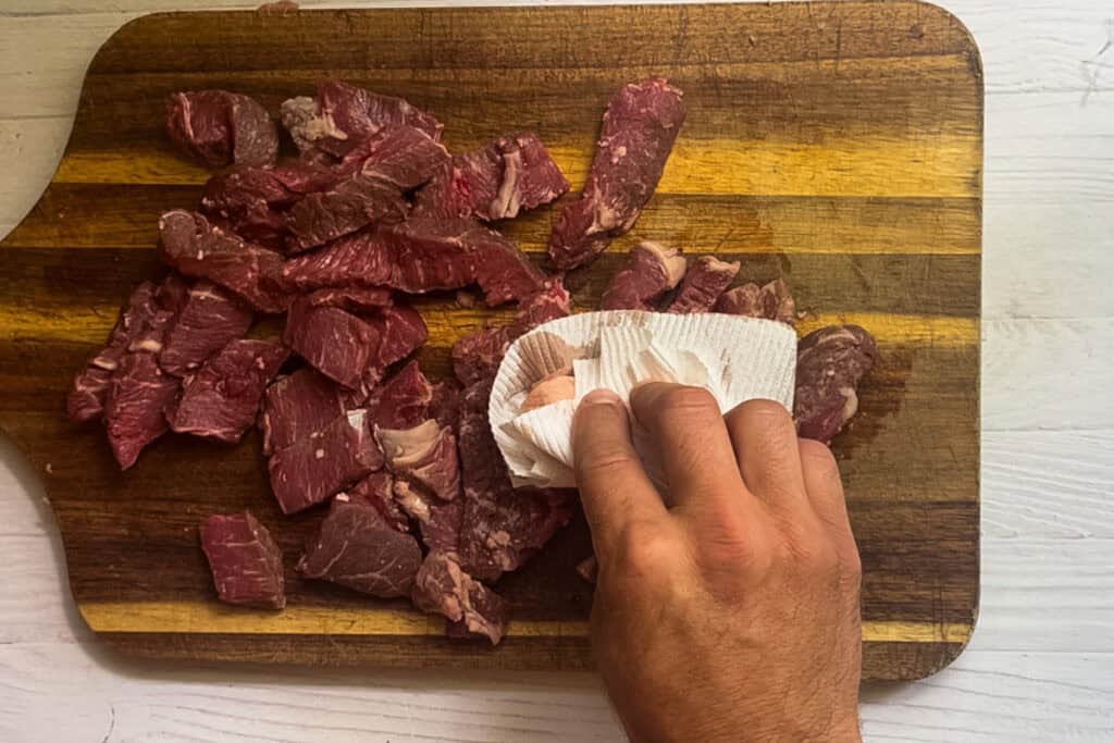 Patting chopped raw steak with a paper towel.