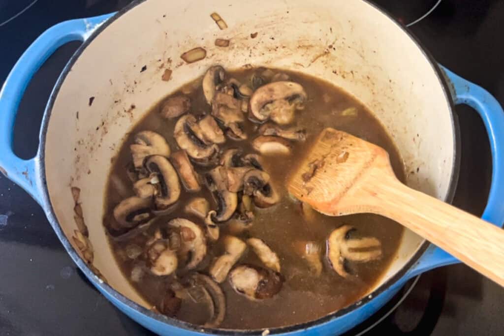 Stirring broth and mushrooms in a dutch oven.