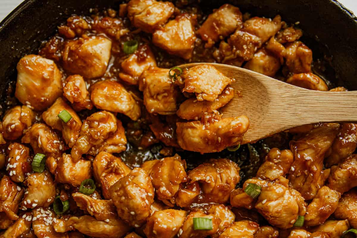 Honey garlic chicken in a cast iron skillet with a wooden spoon.