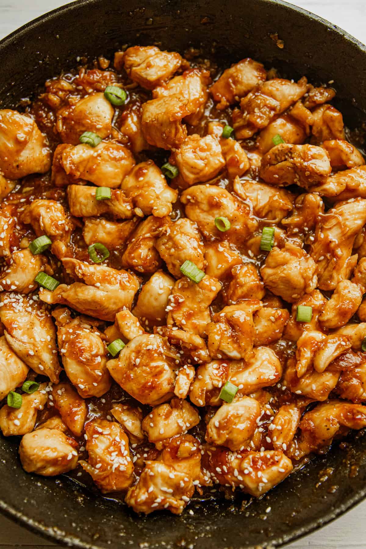 Honey garlic chicken in a cast iron skillet garnished with green onions.
