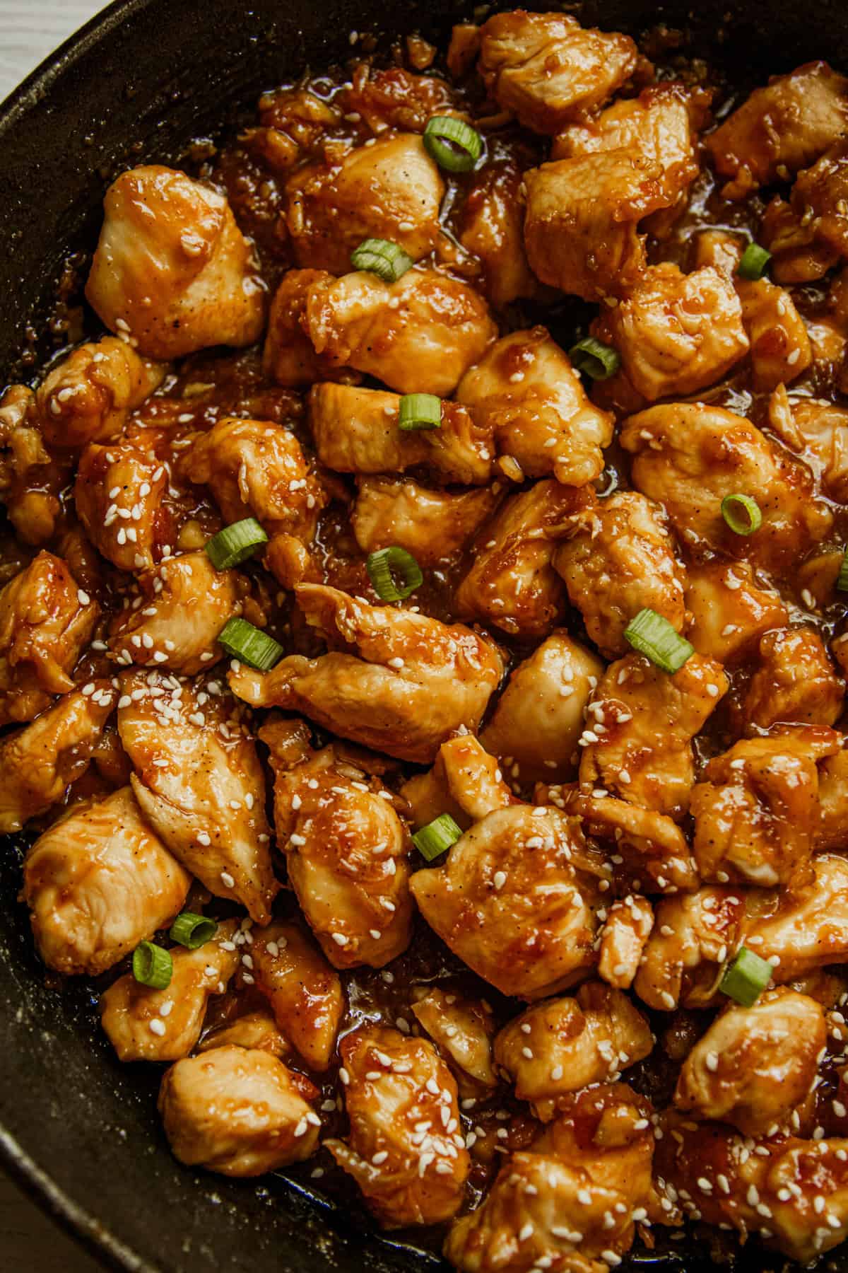 Honey garlic chicken in a cast iron skillet, garnished with green onions.