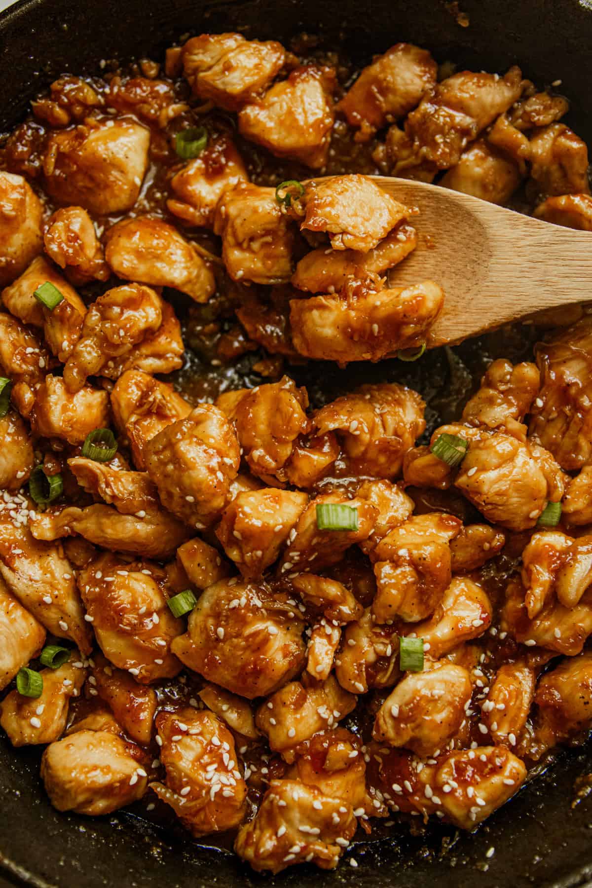 Scooping a spoonful of honey garlic chicken with a wooden spoon.