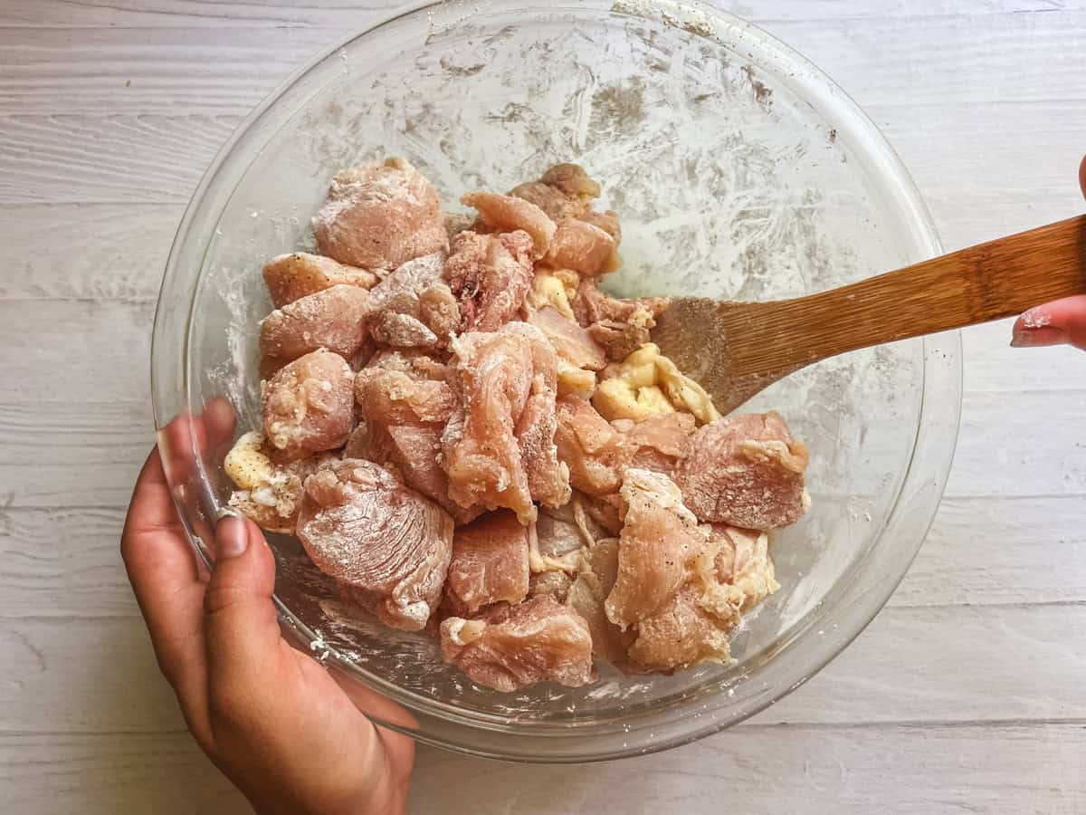 Mixing chicken in a glass bowl with cornstarch and salt and pepper.