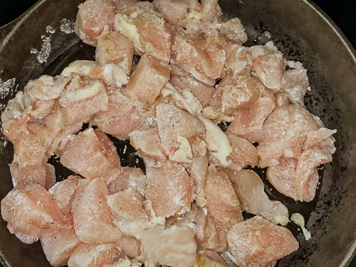 Cooking diced chicken in a cast iron skillet.