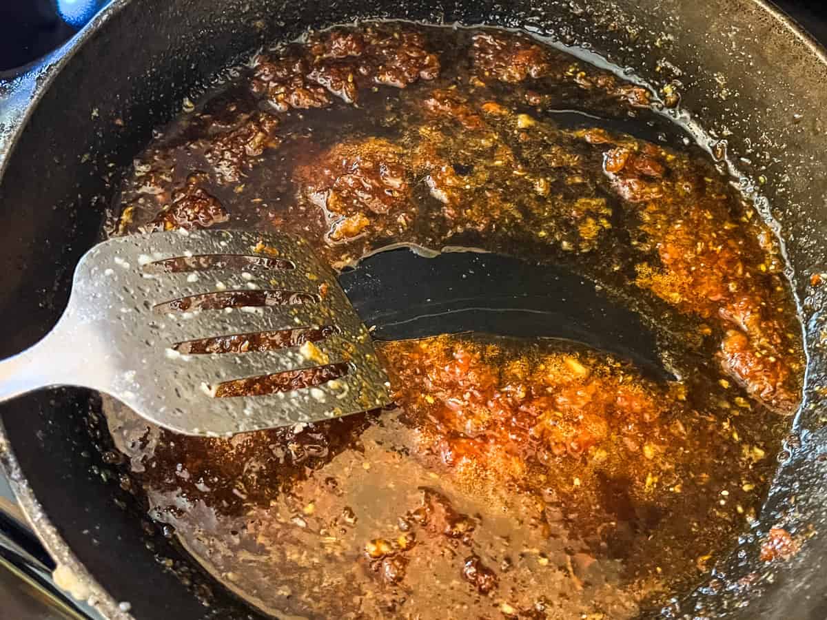 Stirring honey garlic chicken sauce in a cast iron skillet.