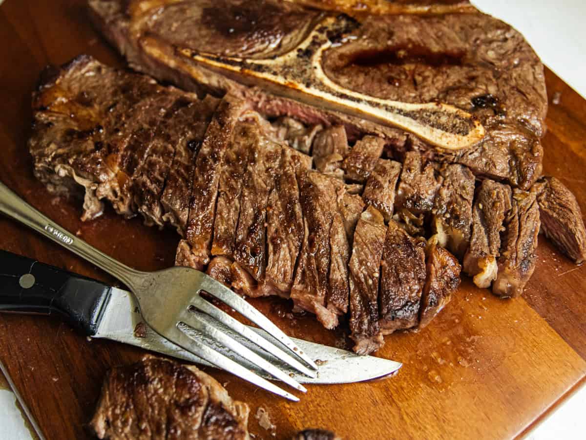 A pan seared chuck steak on a wooden board with a fork and knife.