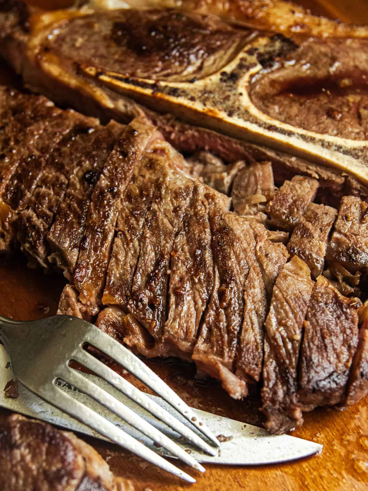 A sliced pan-seared chuck steak on a wooden board with a fork and knife.