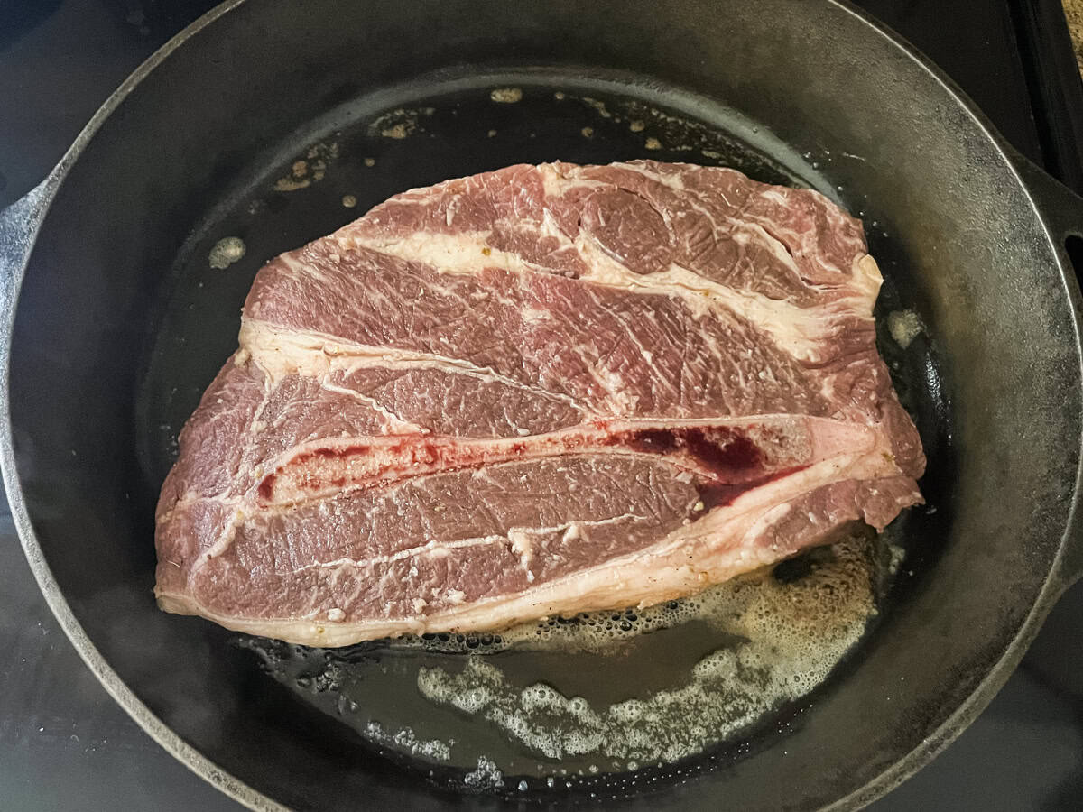 An uncooked chuck steak in a cast iron skillet with melted butter. 