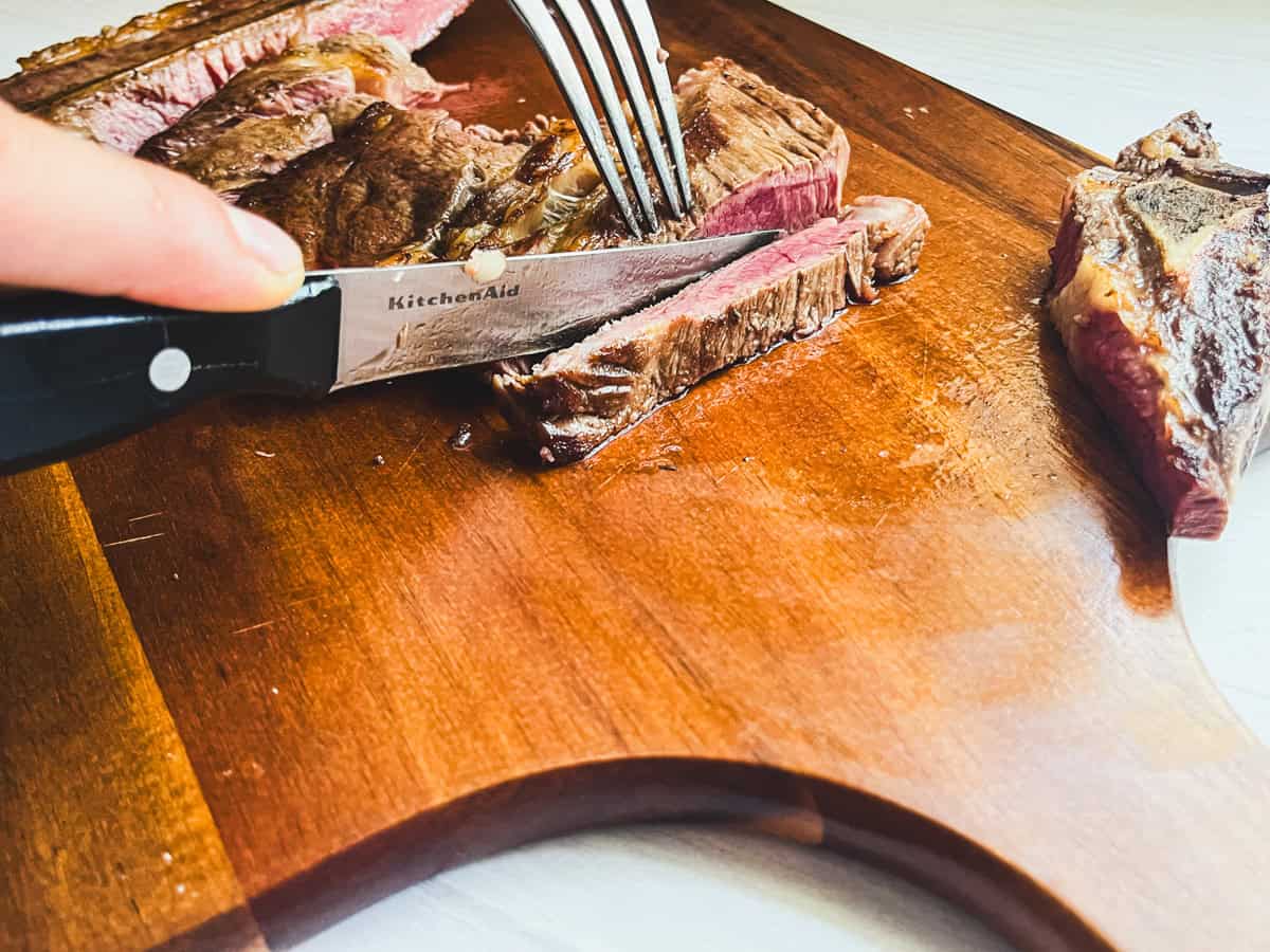 Slicing a seared chuck steak on a wooden cutting board. 