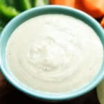 A teal bowl of homemade ranch dressing with fresh veggies in the background.