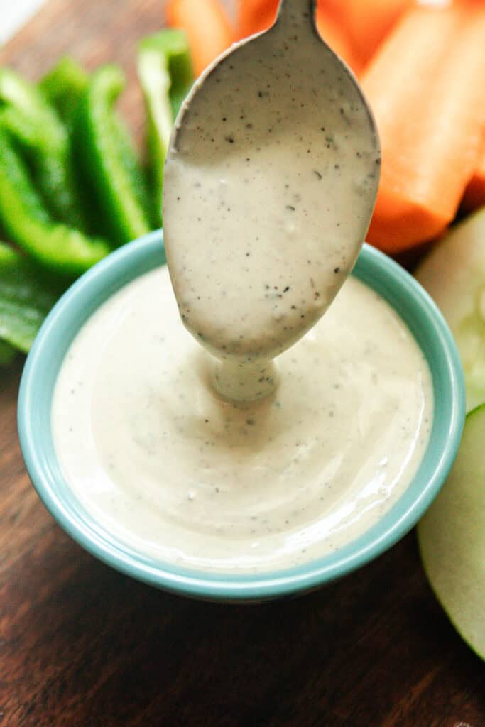 A spoonful of ranch dressing dripping into a blue bowl of ranch.