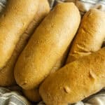Whole grain hot dog buns stacked on a striped towel.