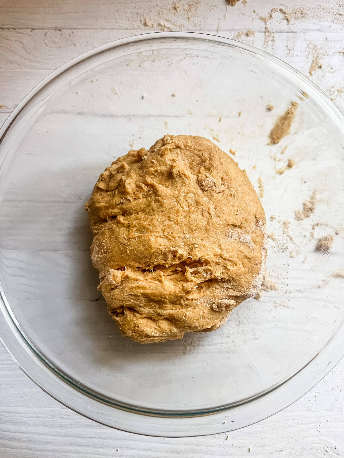 A ball of whole grain hot dog bun dough in a glass bowl rising.