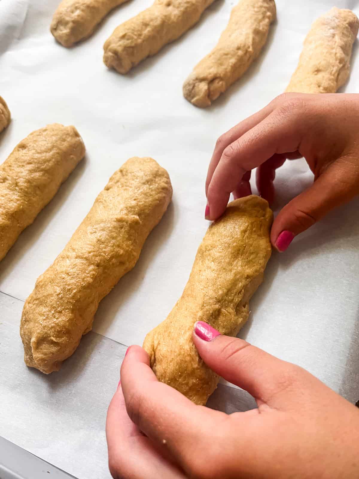 Shaping hot dog bun dough into long bun shapes.