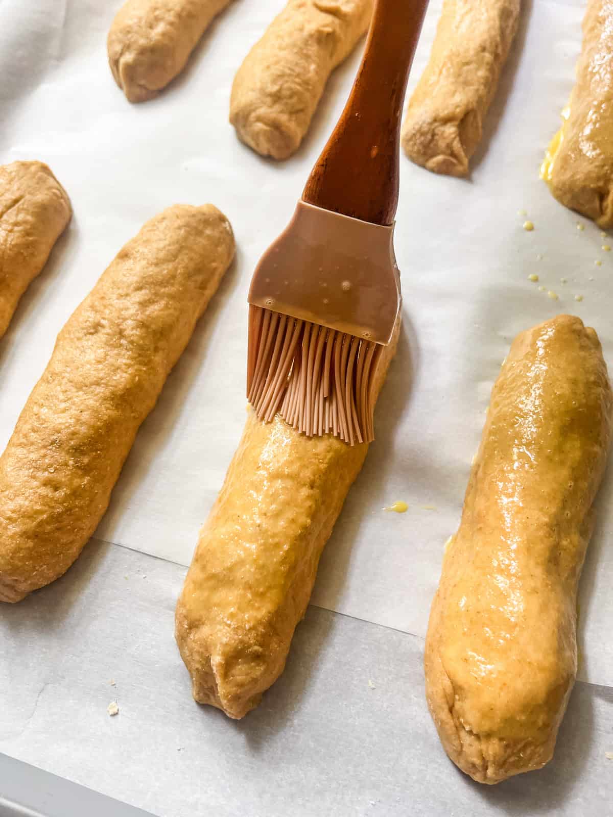 Brushing an egg wash onto unbaked hot dog buns.