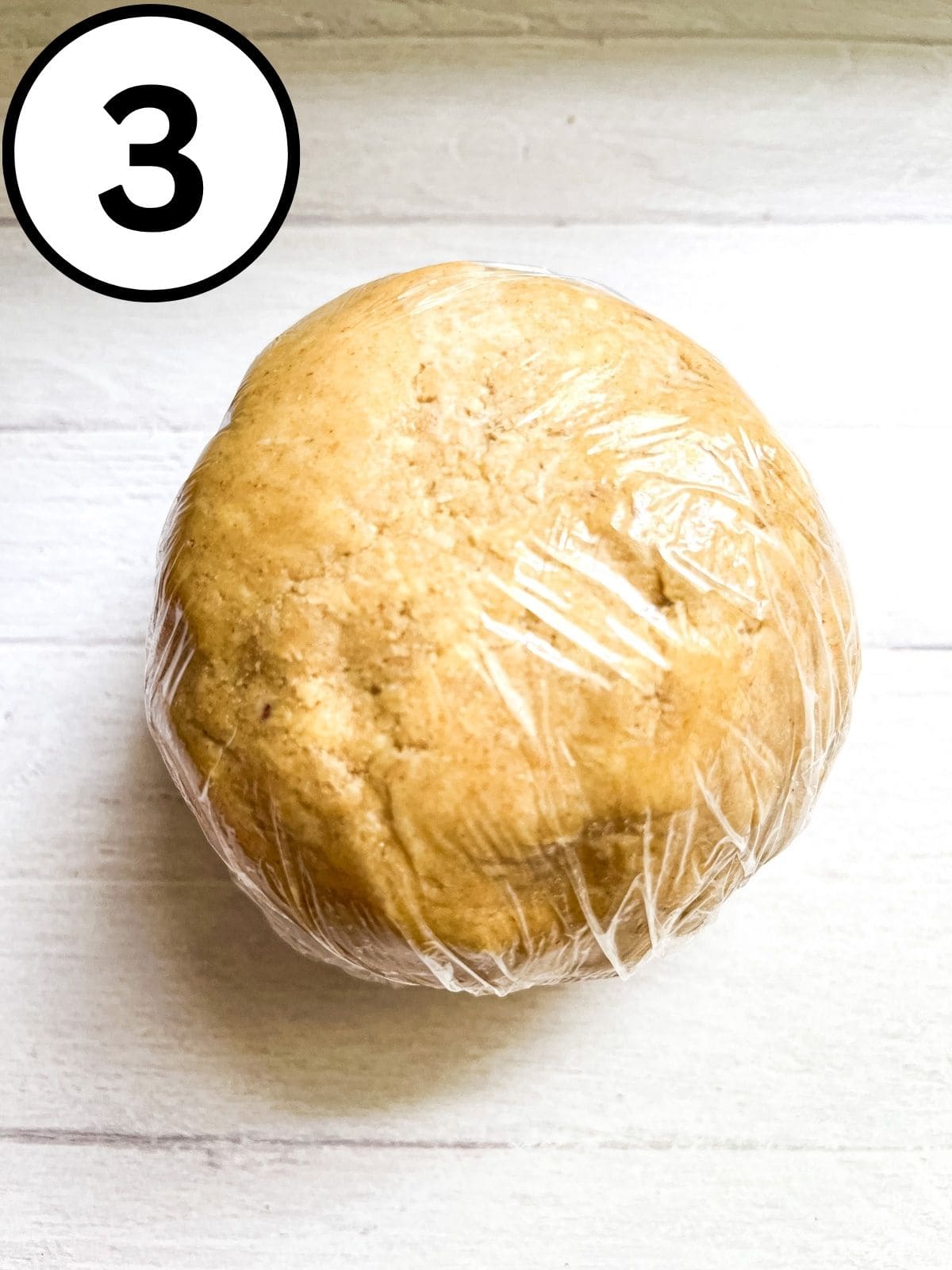 A ball of whole wheat pie dough wrapped in plastic wrap.