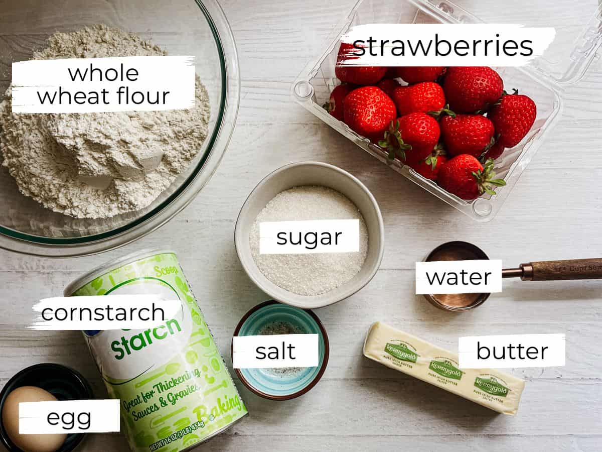 Whole wheat pie dough and strawberry pie ingredients labeled on a white table.
