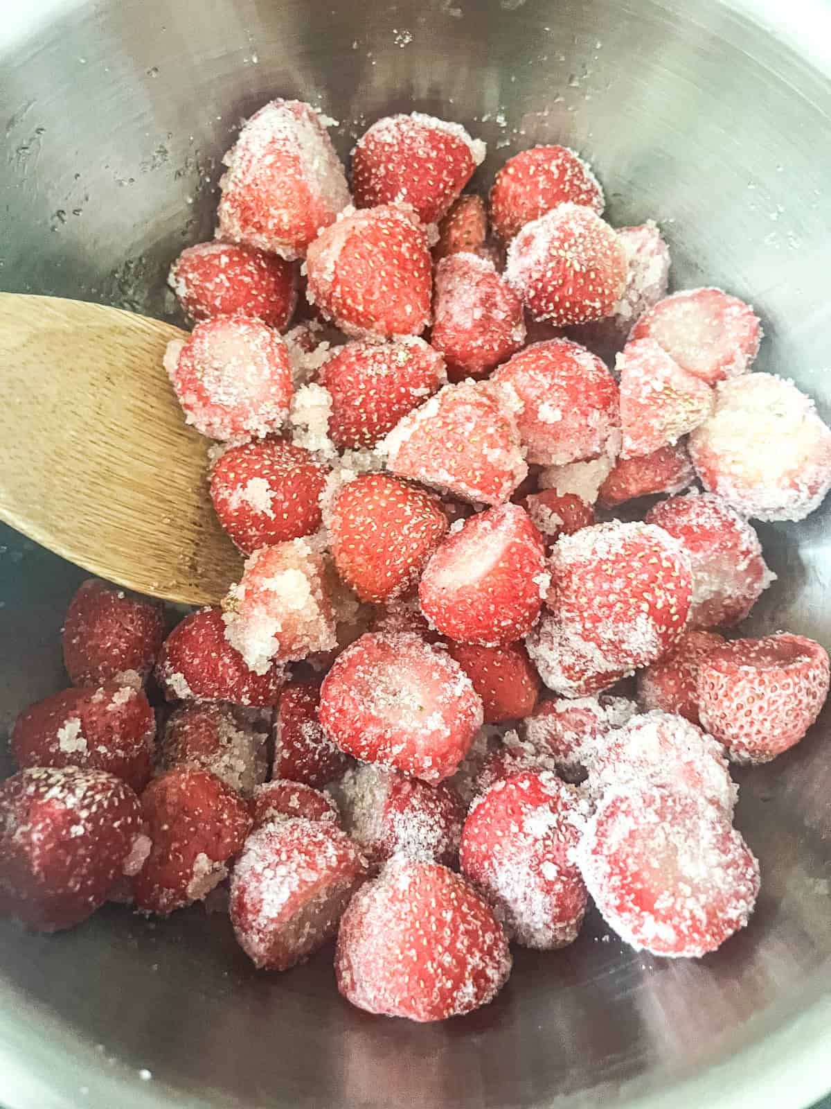 Stirring fresh strawberries with sugar in a metal pot.