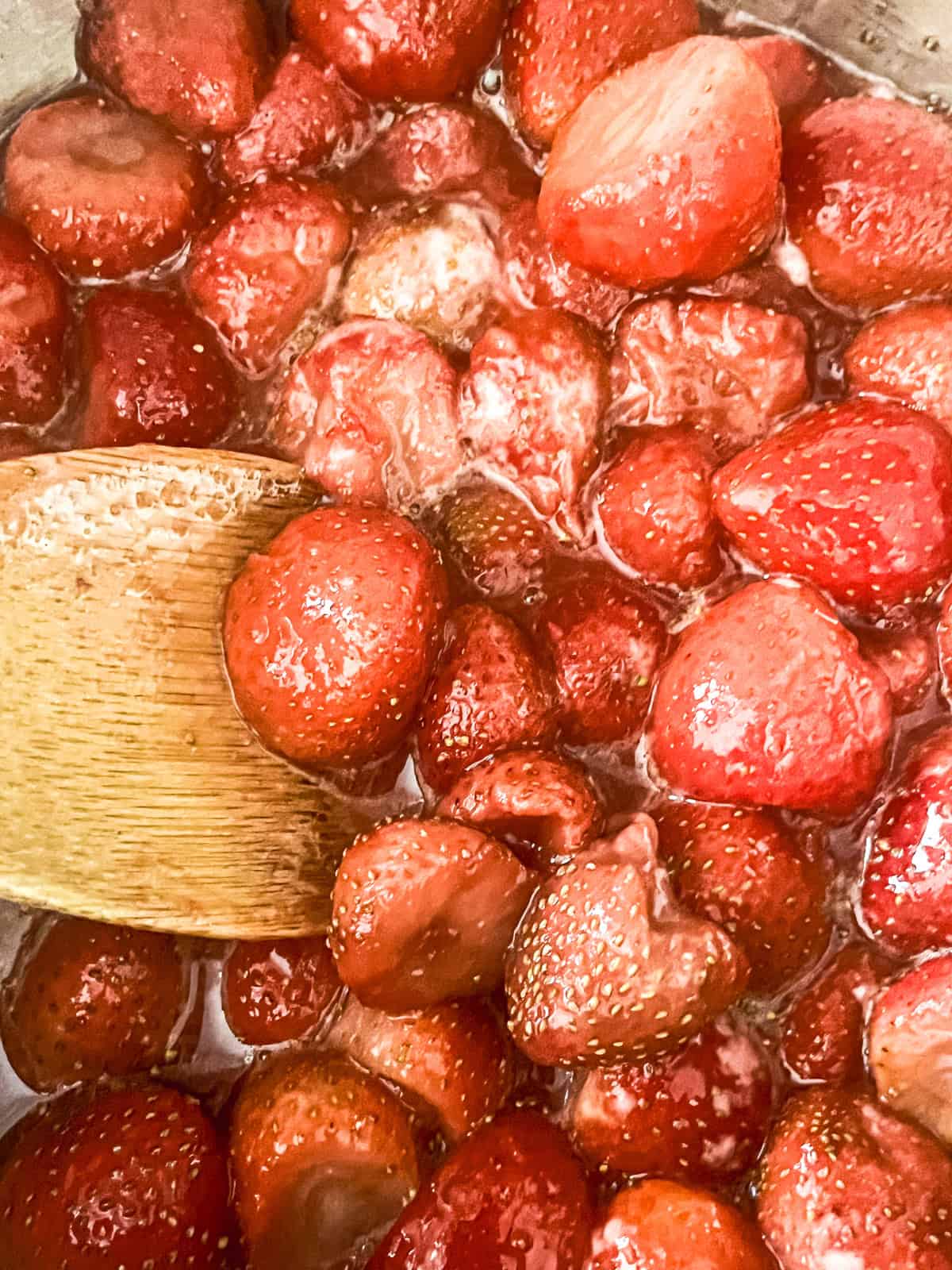 Stirring simmering strawberry pie filling with a wooden spoon.