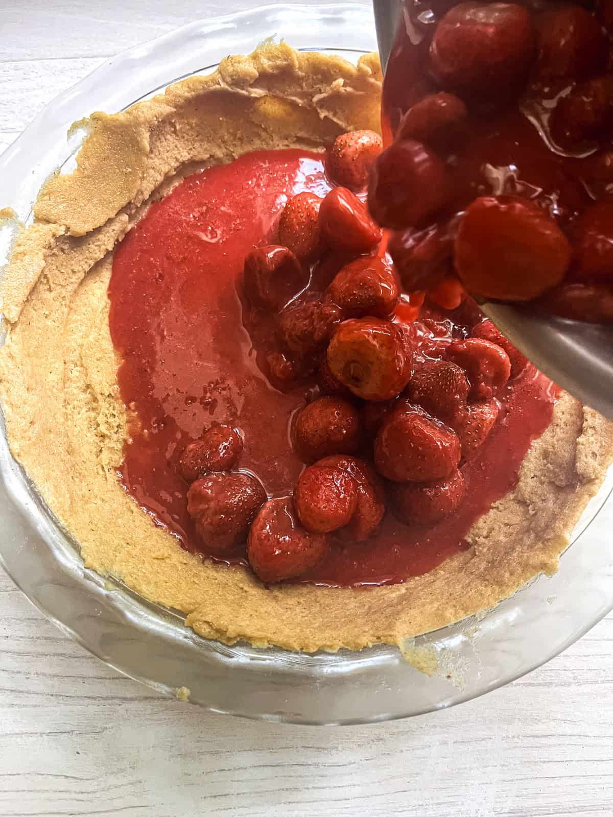 Pouring strawberry pie filling into a whole wheat pie crust.