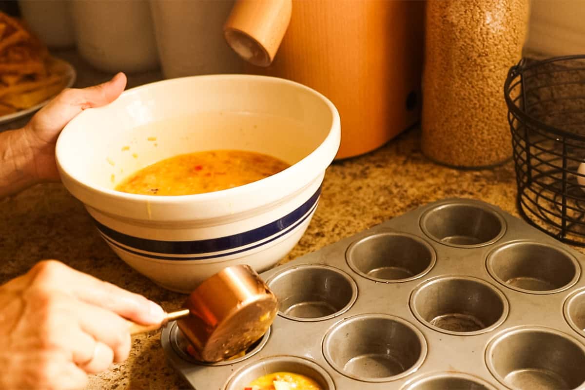 Using a measuring cup to spoon egg mixture into a muffin tin. 