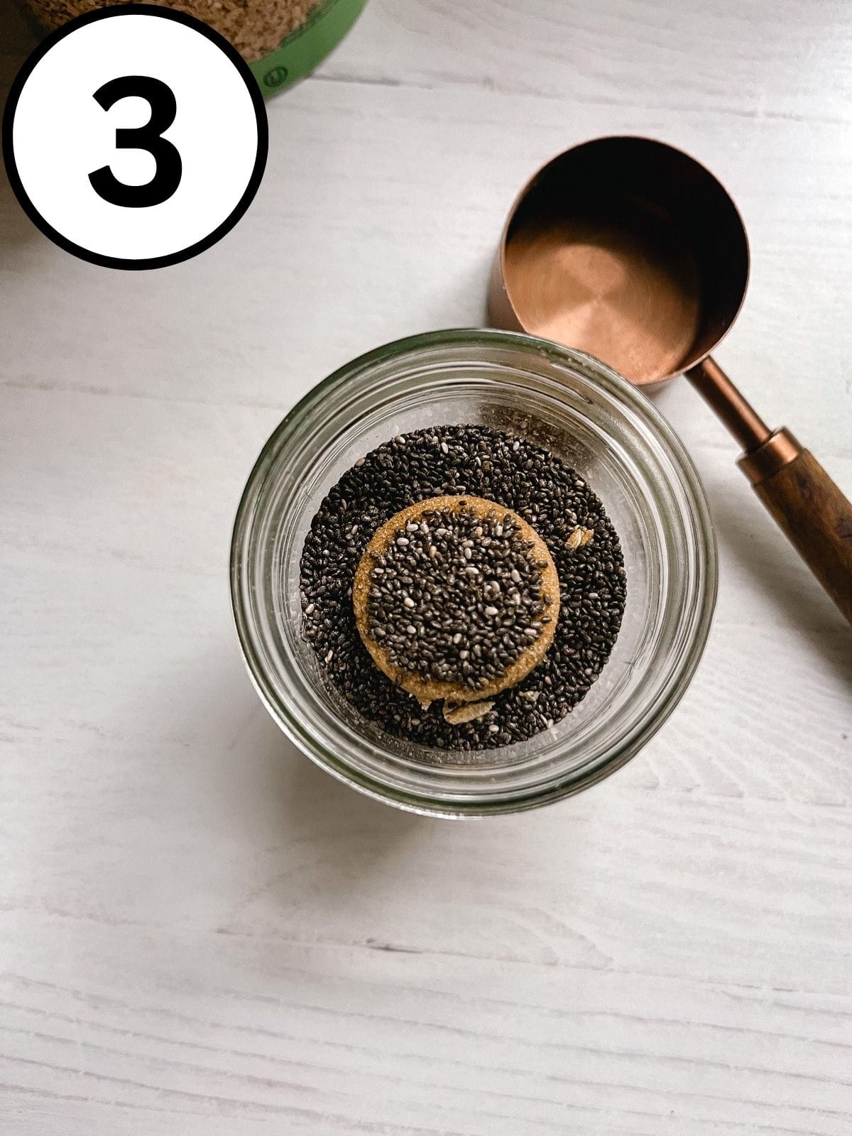 Chia seeds added on top of other ingredients in a mason jar.