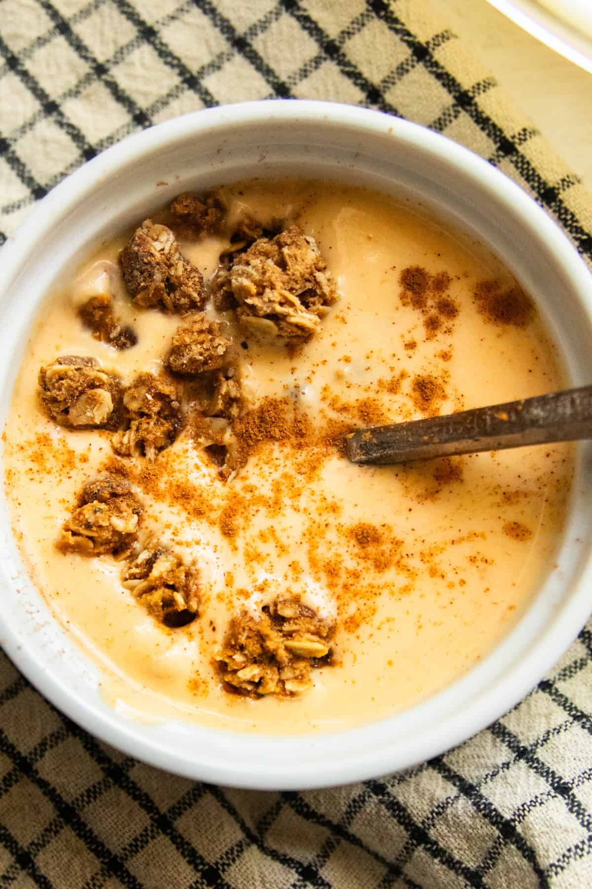 A bowl of pumpkin yogurt topped with granola on a checkered placemat.