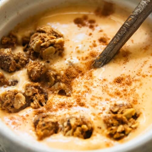 A bowl of pumpkin yogurt with granola on a checkered placemat.