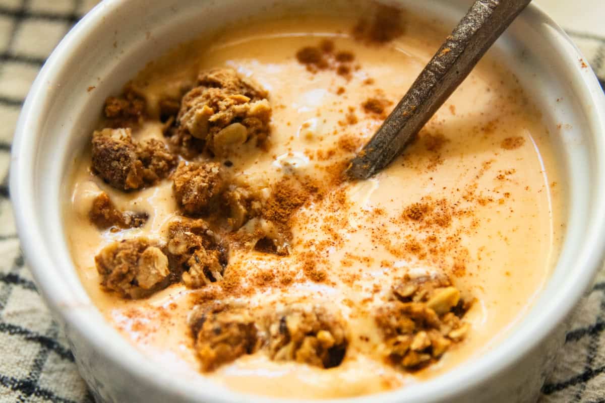 A bowl of pumpkin yogurt with granola on a checkered placemat.