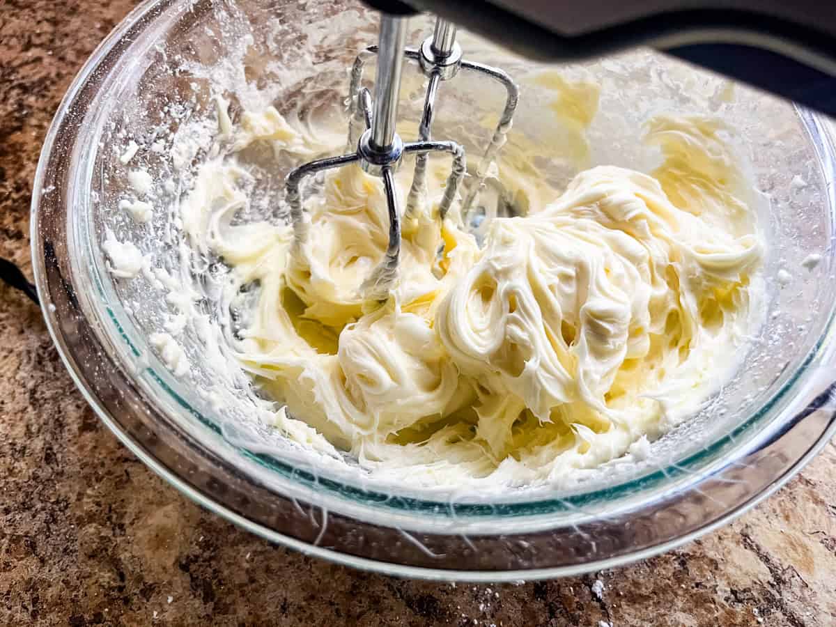 Mixing cream cheese filling in a glass bowl with an electric hand mixer.