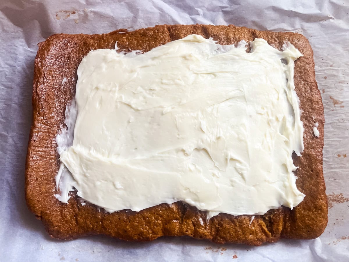 Spreading cream cheese filling on the unrolled pumpkin bread.