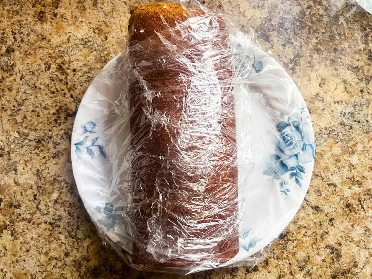 Pumpkin roll wrapped in plastic wrap on a plate.