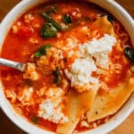 A white bowl filled with lasagna soup with a spoon in it.
