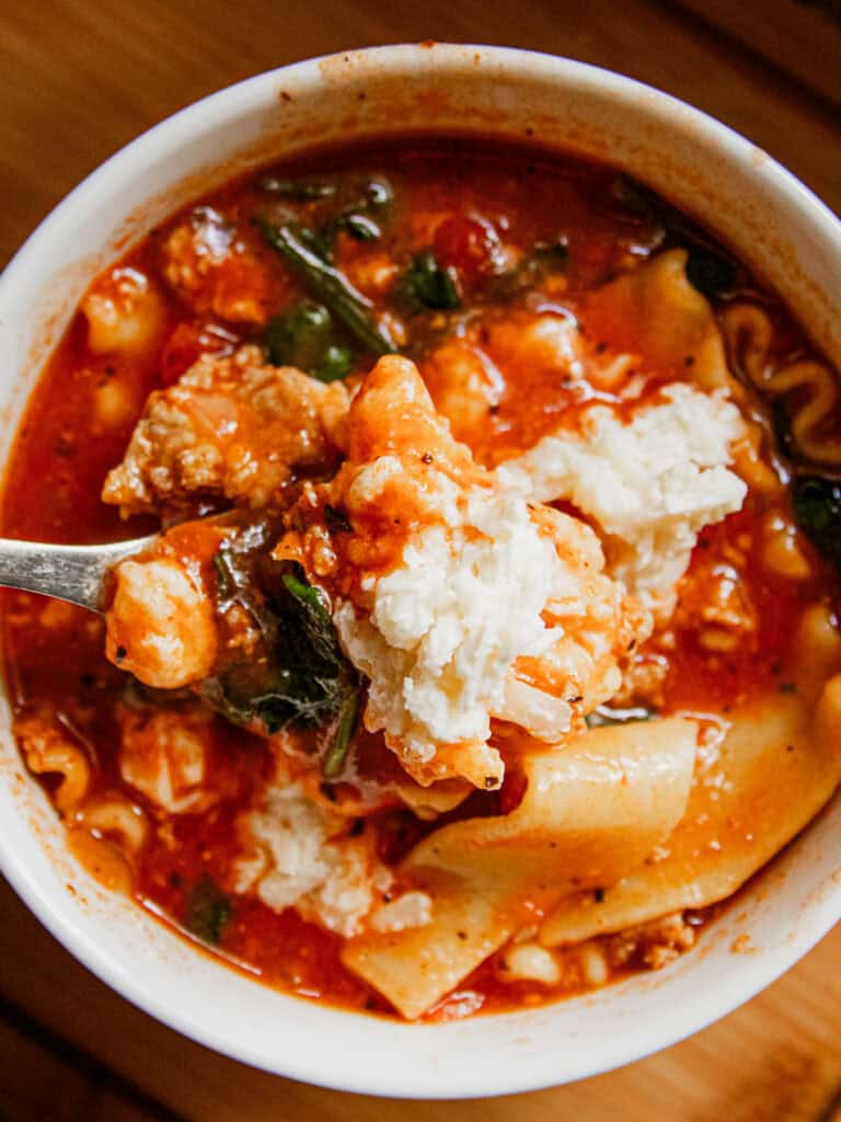 A white bowl filled with lasagna soup with a spoon in it.