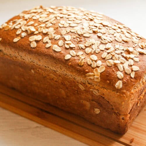A loaf of seeded whole grain bread on a wooden cutting board.