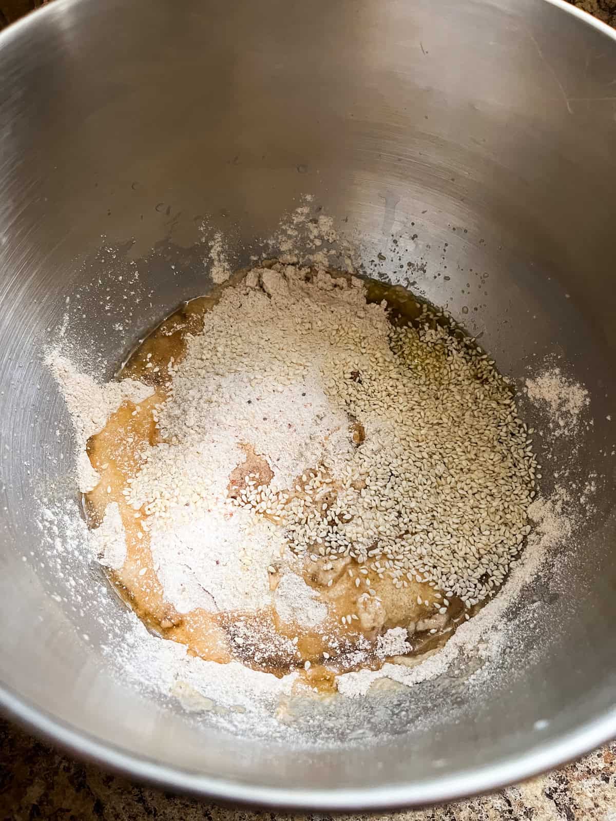 Adding other ingredients into a mixing bowl with yeast, milk, and water in it.