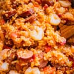 A close-up of dutch oven jambalaya in a white bowl with a wooden spoon.