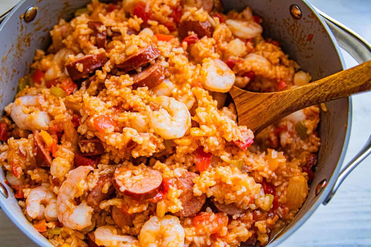 A Dutch oven with jambalaya and a wooden spoon in it.