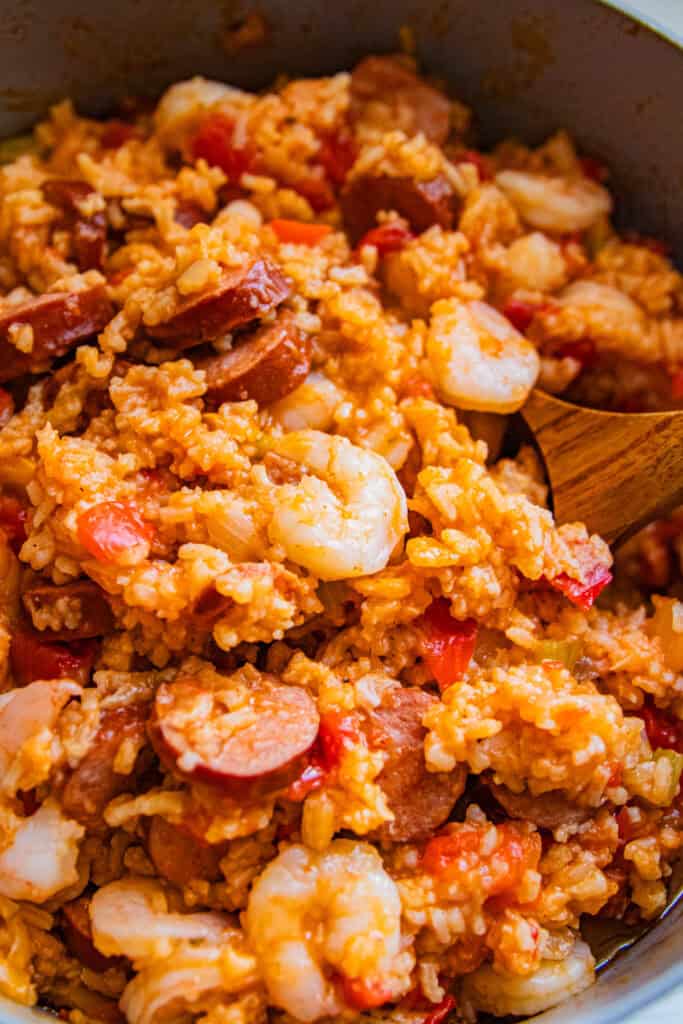A close-up of dutch oven jamabalaya with a wooden spoon in it.