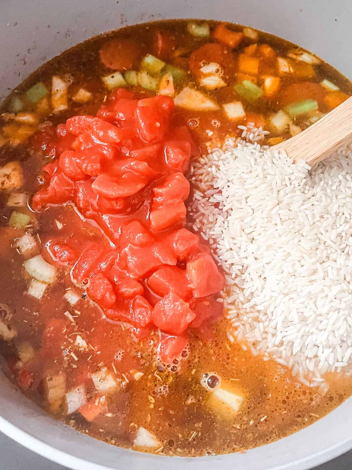Rice, broth, and diced tomatoes added to a dutch oven of jambalaya.