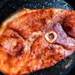 Ham steak in a cast iron skillet with a sweet and spicy glaze.