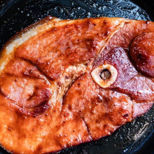 Ham steak in a cast iron skillet with a sweet and spicy glaze.