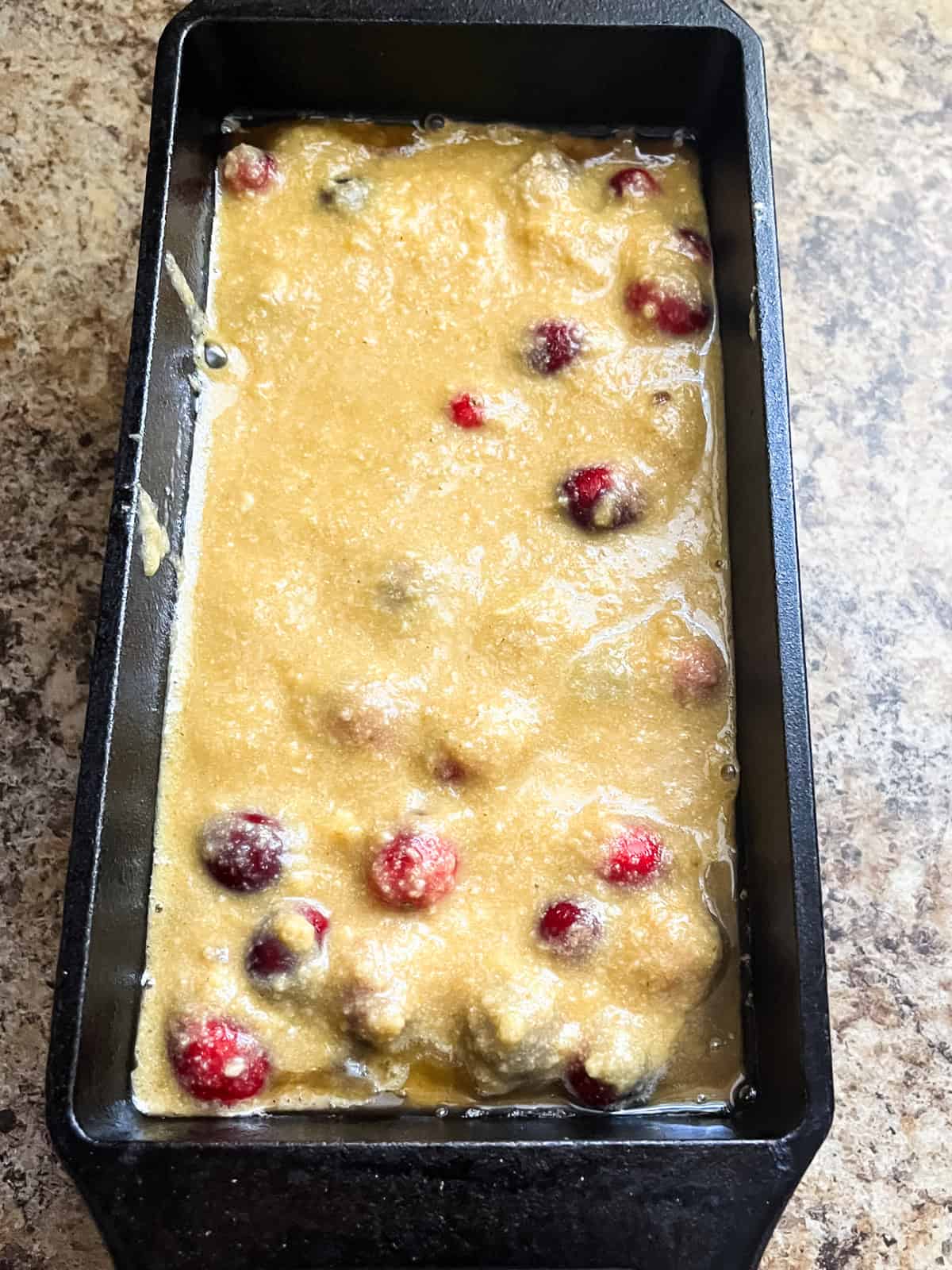 Unbaked cranberry bread in a loaf pan with fresh cranberries in it.