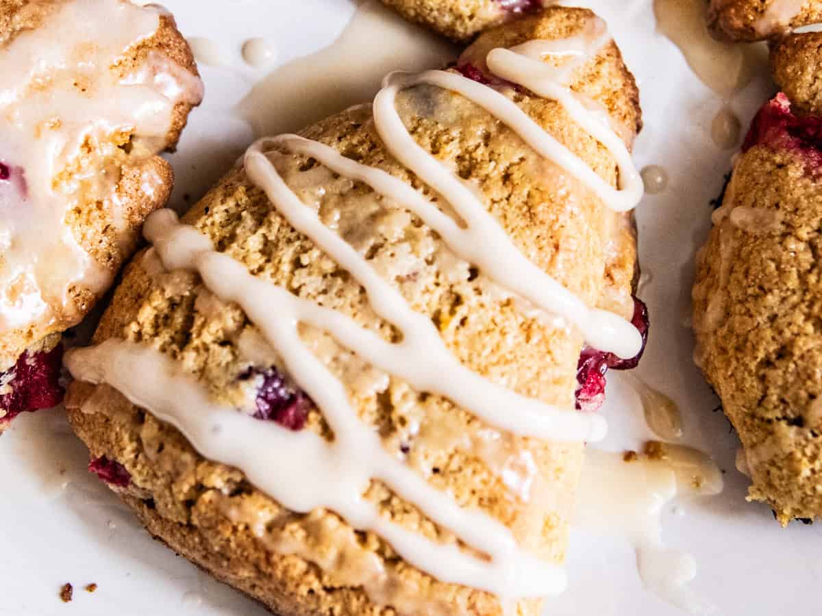 Whole grain cranberry orange scones with glaze on a white plate.