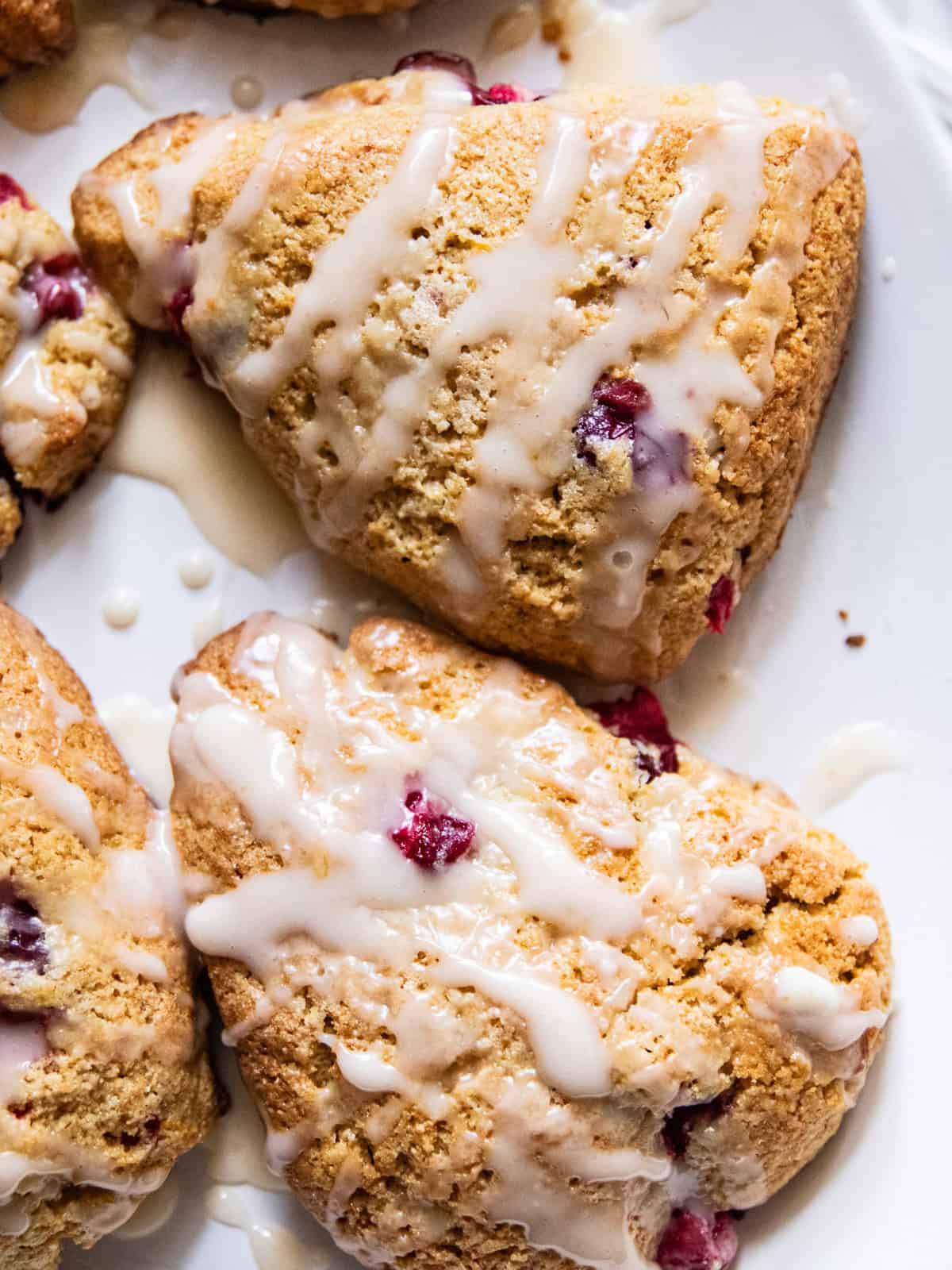Freshly milled cranberry orange scones drizzled with orange glaze on a white plate.